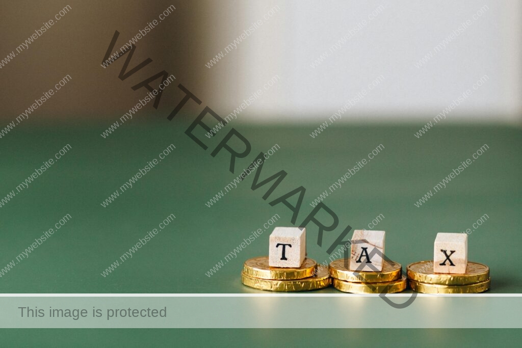 pexels-photo-6863186-6863186 Stacked gold coins with wooden blocks spelling 'TAX' on a green backdrop.